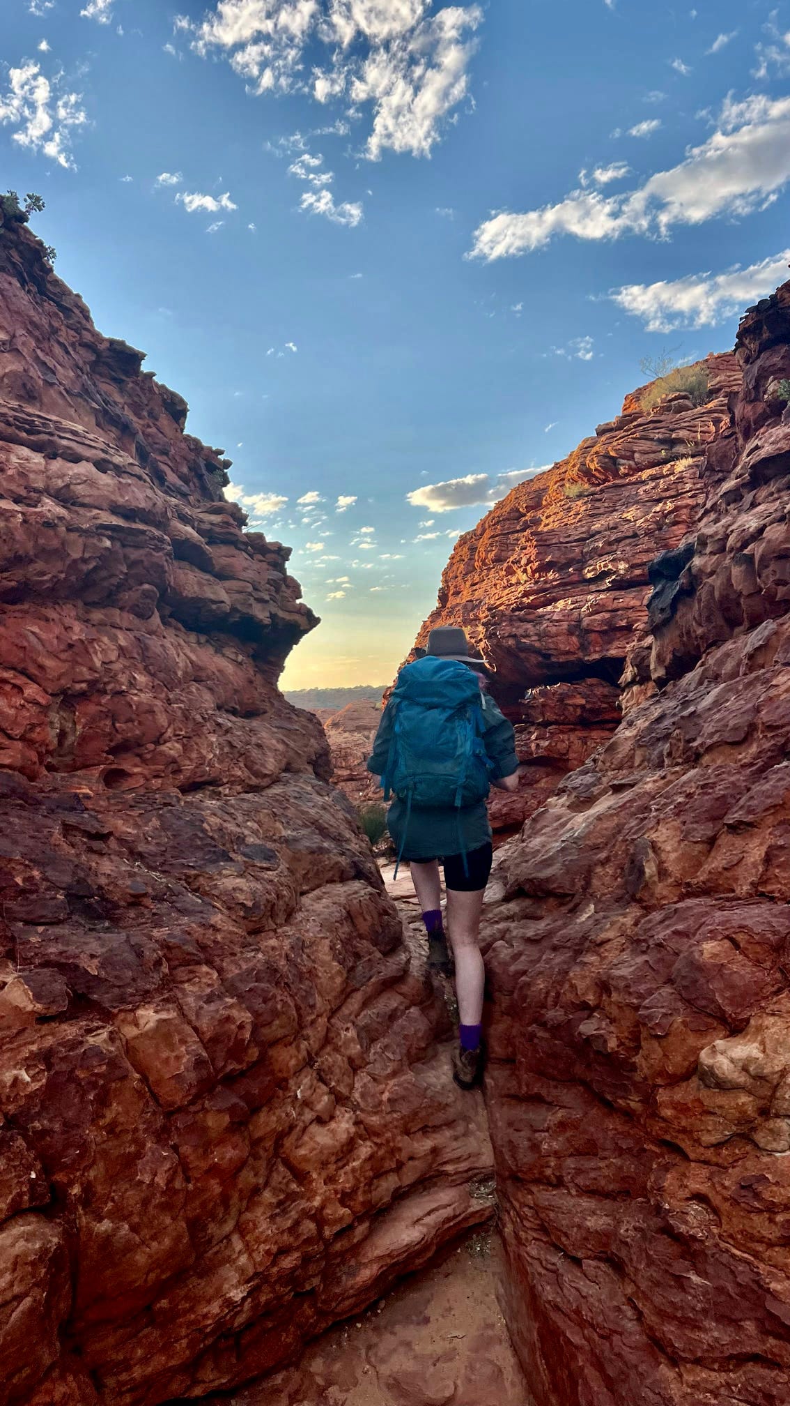 A determined hiker makes their way through a narrow passage between towering red rocks at Kings Canyon, capturing the adventure and natural beauty of the area.