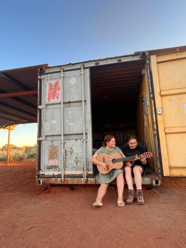 Tour participants enjoy a relaxed moment playing the guitar at the campsite, sitting on the edge of a shipping container.