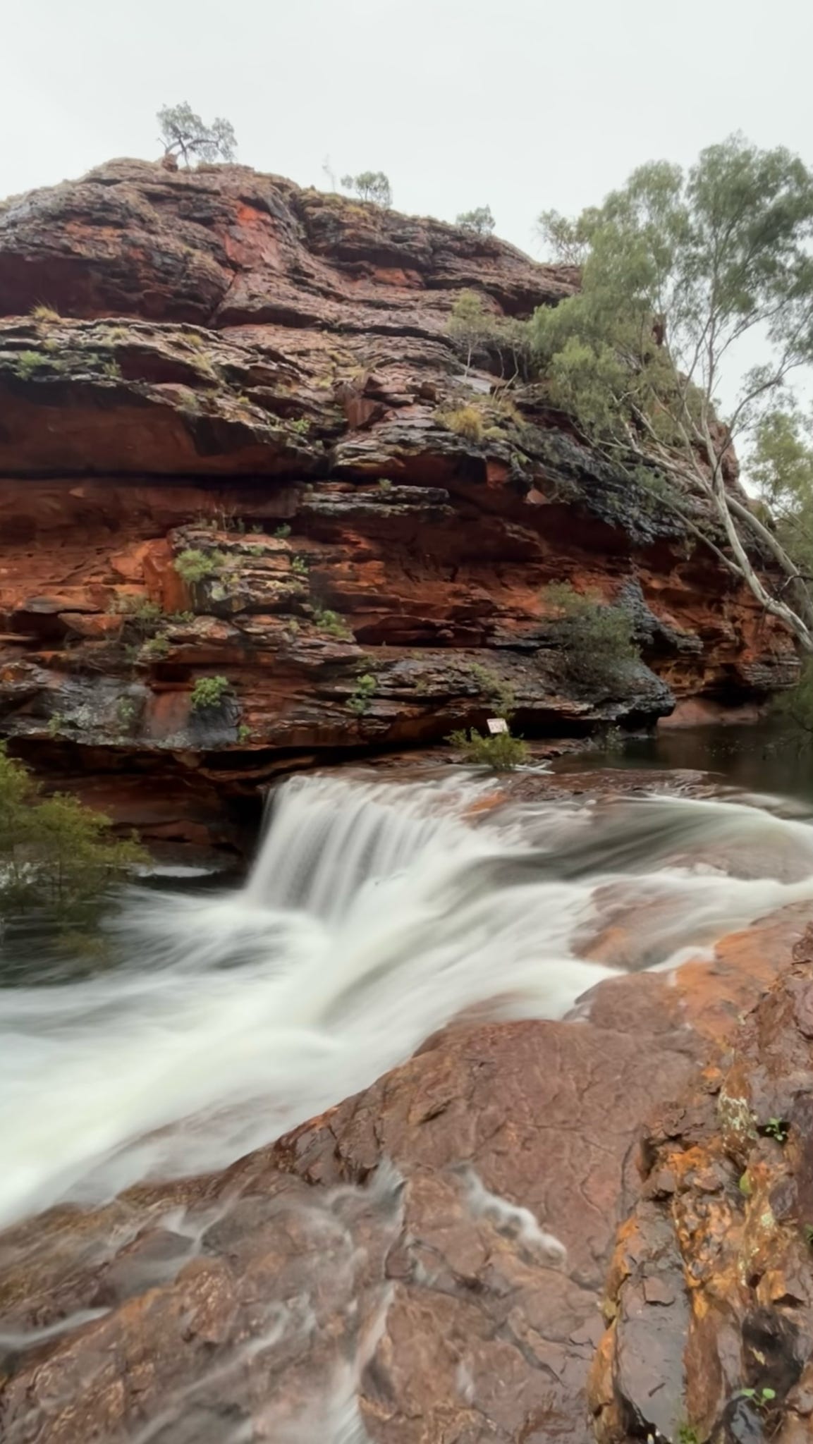 A stunning waterfall flows over the rocks at Kings Canyon, providing a serene and picturesque scene amidst the rugged landscape of the Australian outback.