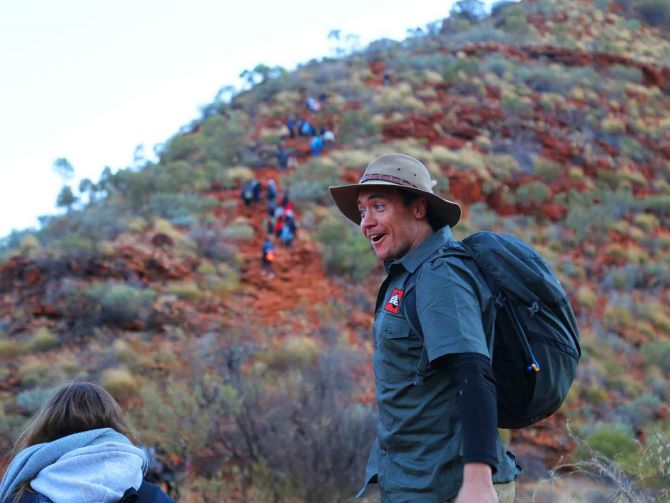 A Mulgas Adventures tour guide leads a group hike at Kings Canyon, exuding energy and excitement amidst the rugged beauty of the Australian outback.