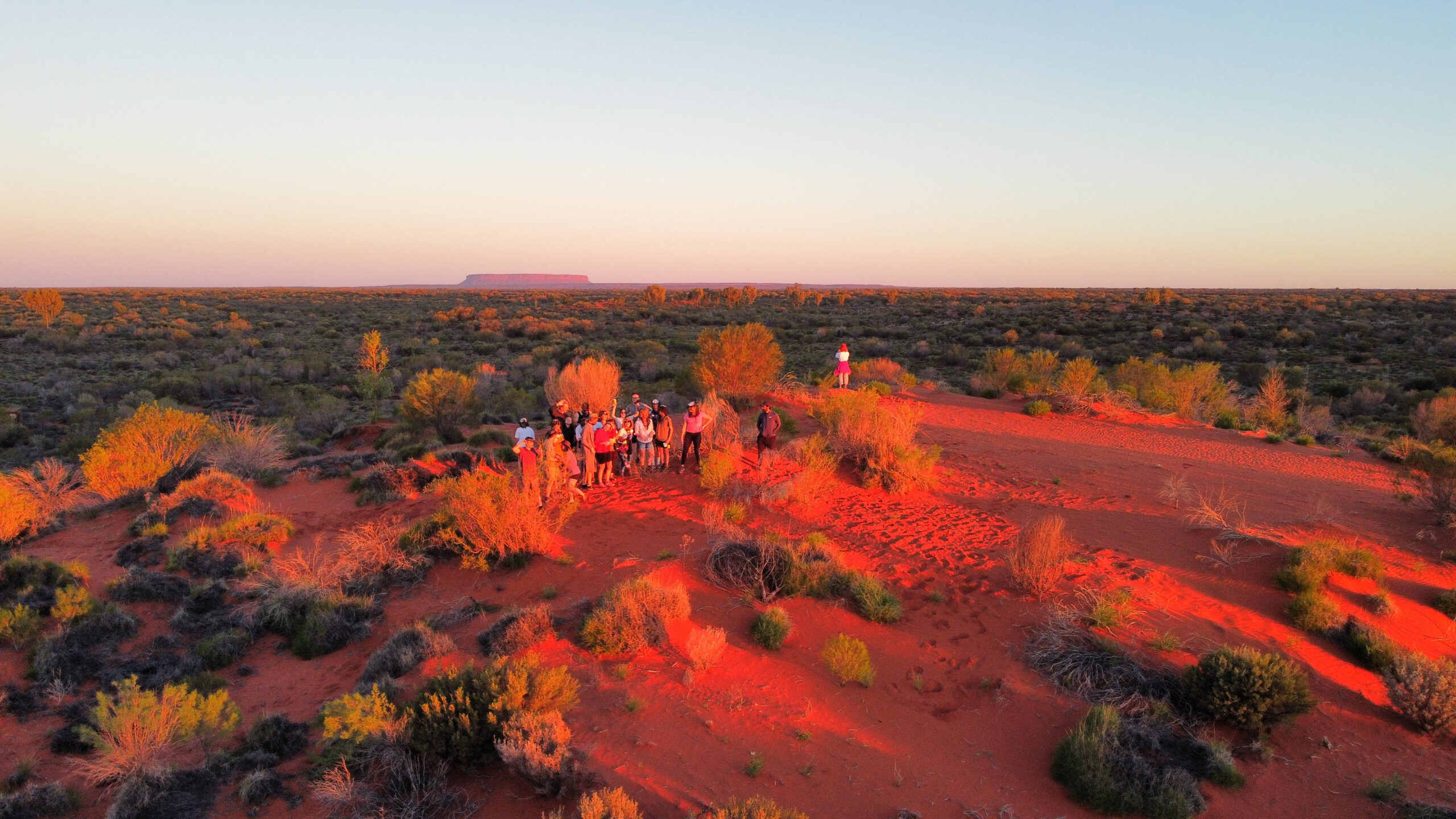 A group of Mulgas Adventures tour group explores the vibrant red sand dunes of the Australian outback at sunset, capturing the essence of adventure and natural beauty.