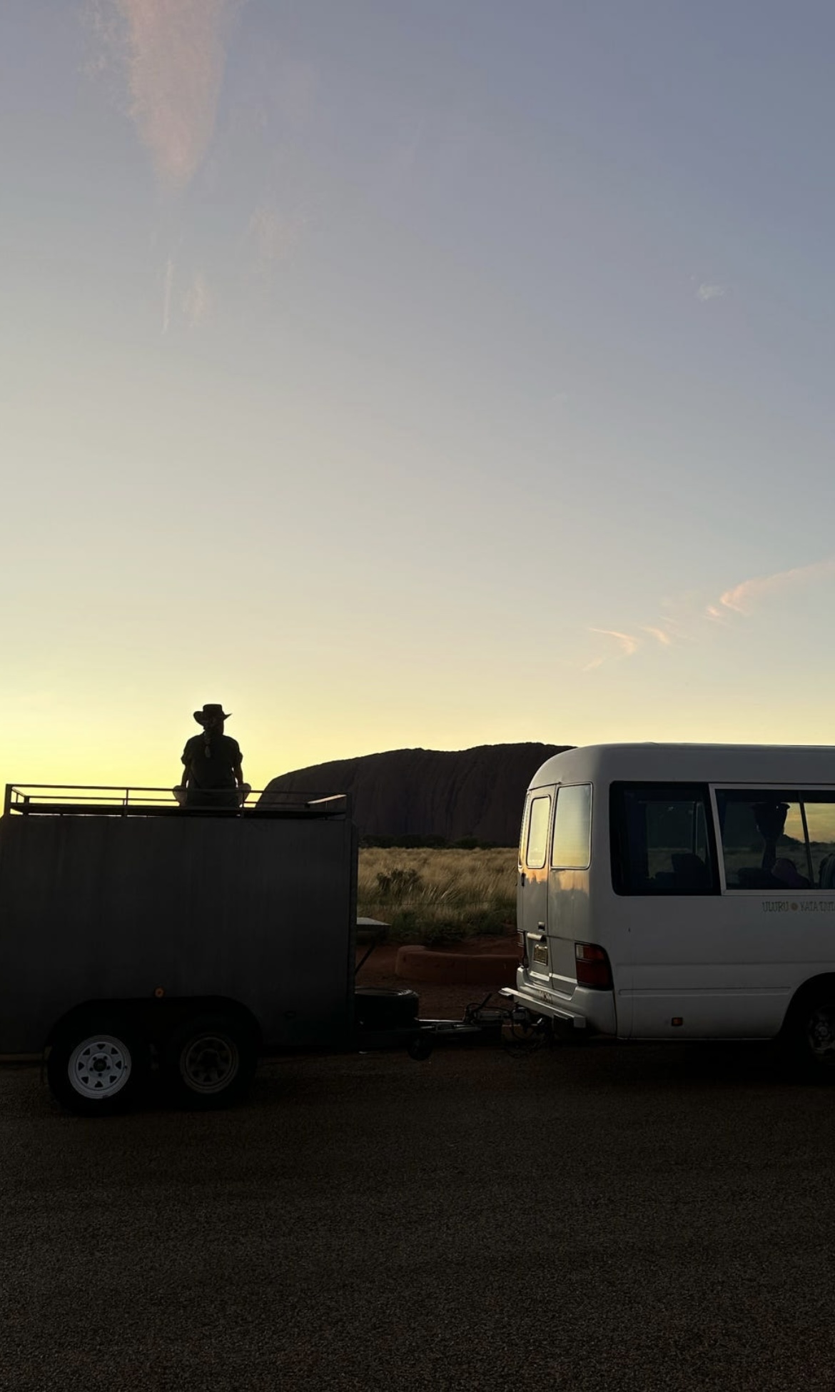 A serene moment captured at sunrise with a tour guide silhouetted against the iconic Uluru, showcasing the tranquil beauty of Central Australia with Mulgas Adventures.