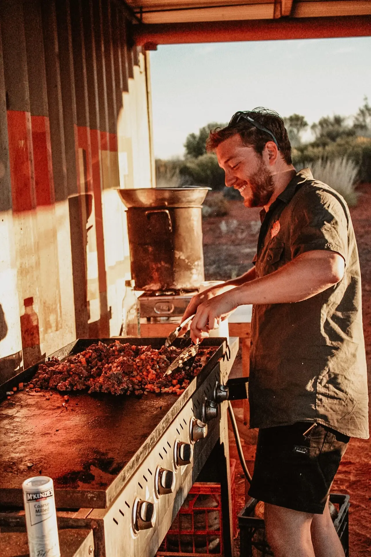 Mulgas Adventures tour guide Alex prepares a delicious meal at a campsite in the Australian outback, showcasing the authentic and immersive experiences of the tour.