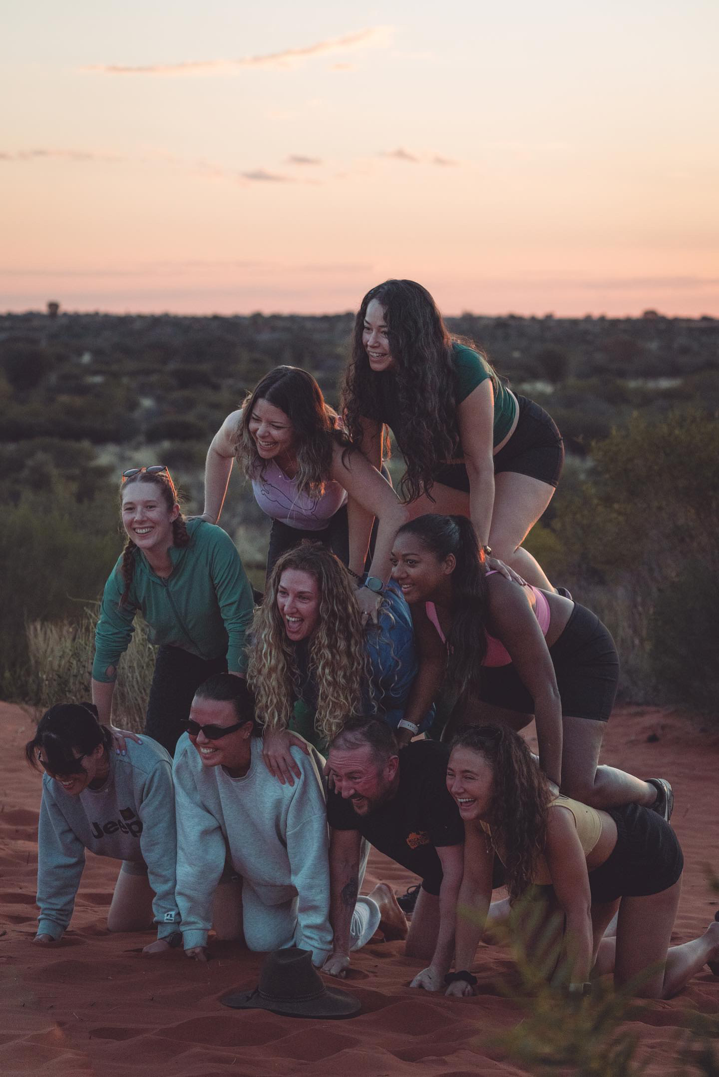 A group of travelers on a Mulgas Adventures tour forming a human pyramid at their campsite in the Australian outback, capturing the spirit of adventure and camaraderie. Photo credit: Nastasia Klopp. Instagram: @nastasiaklopp