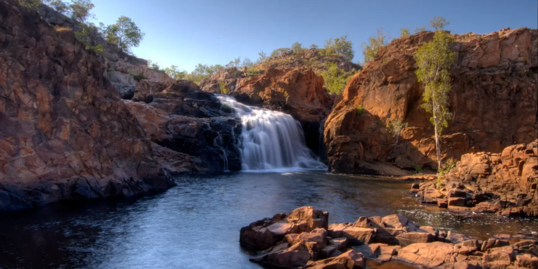 Edith Falls cascading into a serene pool surrounded by rocky cliffs and greenery.